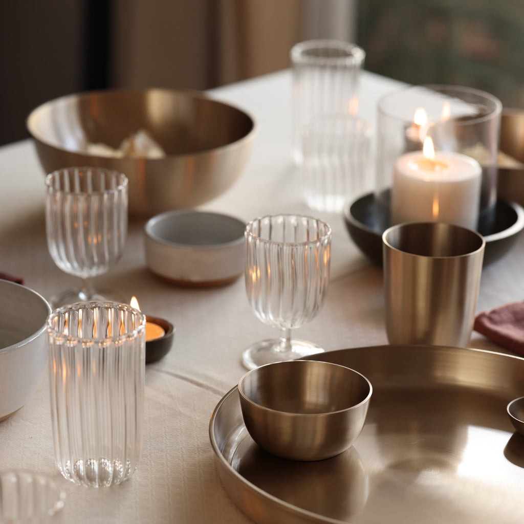 Table setting with metallic bowls, glassware, and candles on a neutral background