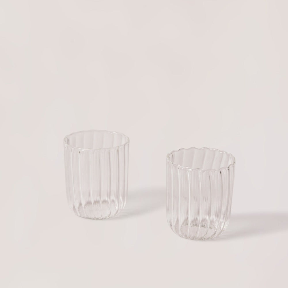 Two clear glass tumblers with ribbed design on a light gray background