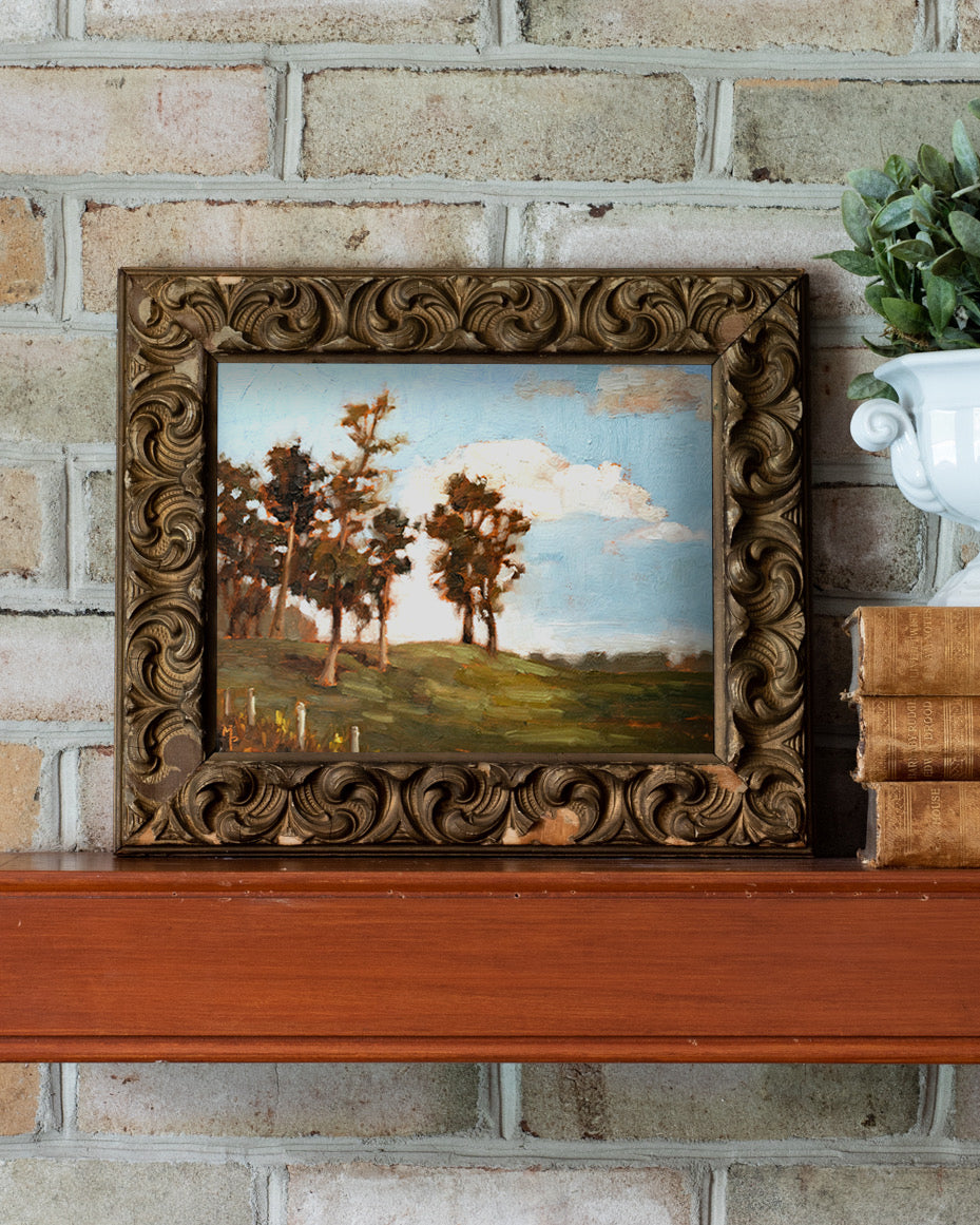 Framed painting of a landscape with trees on a brick wall