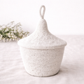 Handwoven white lidded storage basket with a decorative loop handle and textured artisan design.