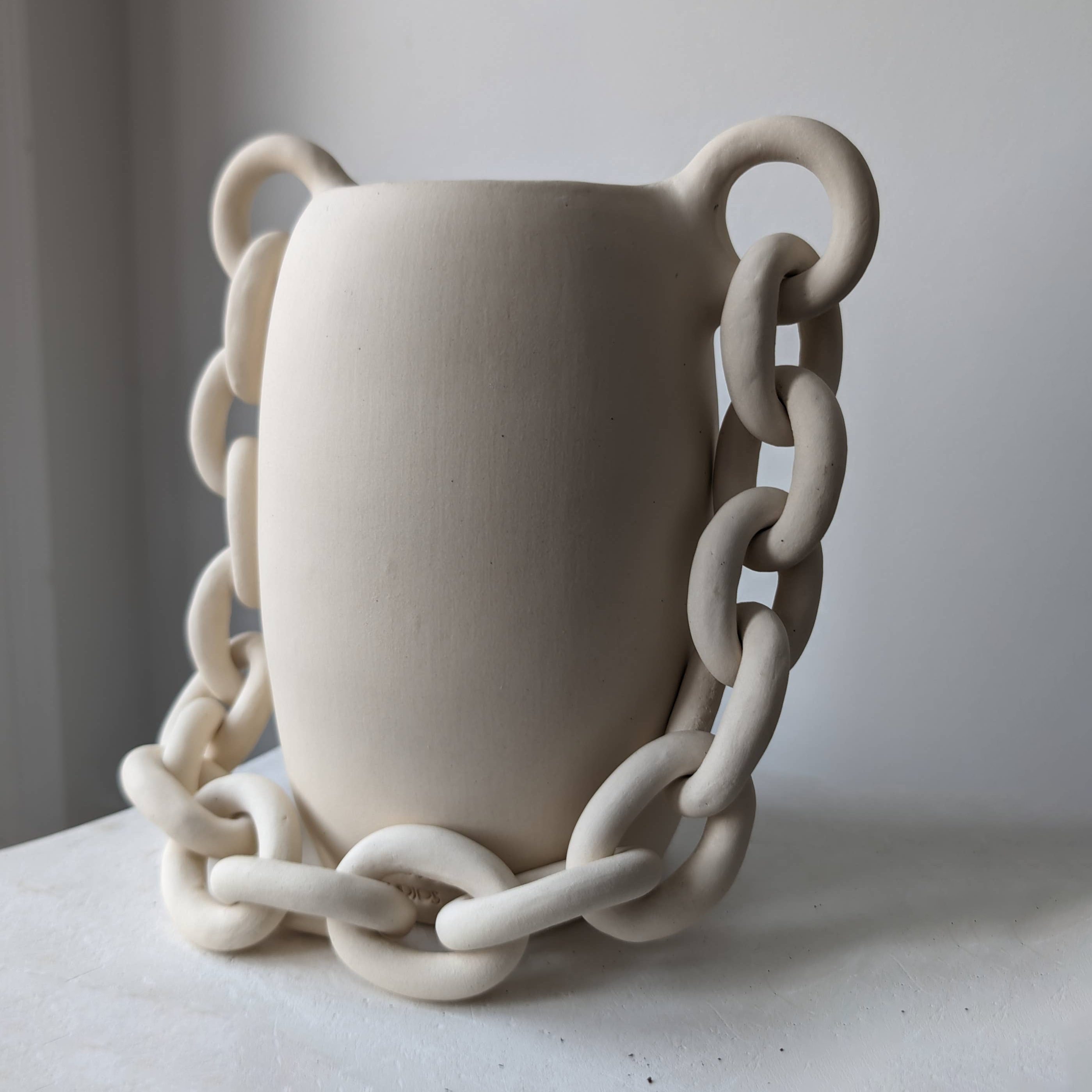 White ceramic vase with chain-like handles on a neutral background
