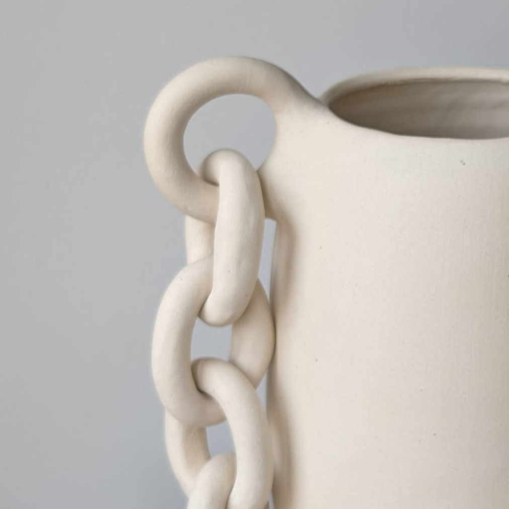 Ceramic vase with chain-like handle on a gray background