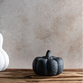 Black pumpkin decoration on a wooden surface with a textured wall background