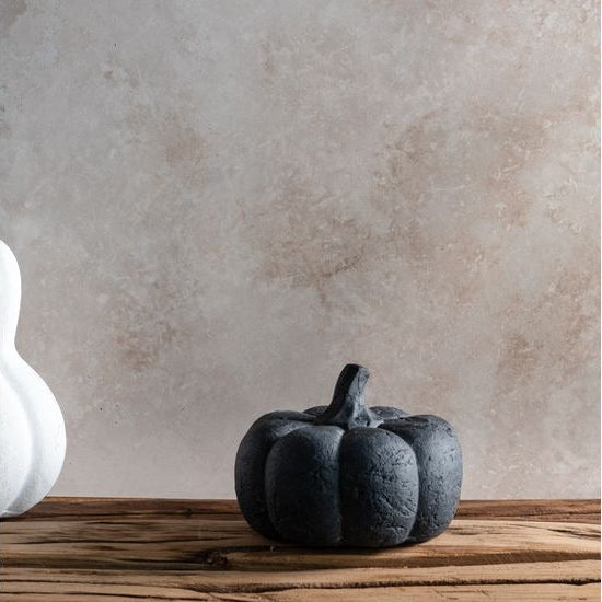 Black pumpkin decoration on a wooden surface with a textured wall background