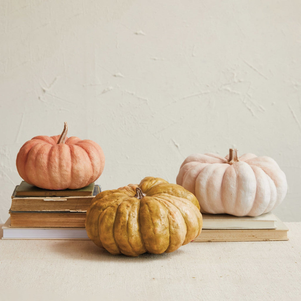 Three pumpkins of different colors on books against a light background