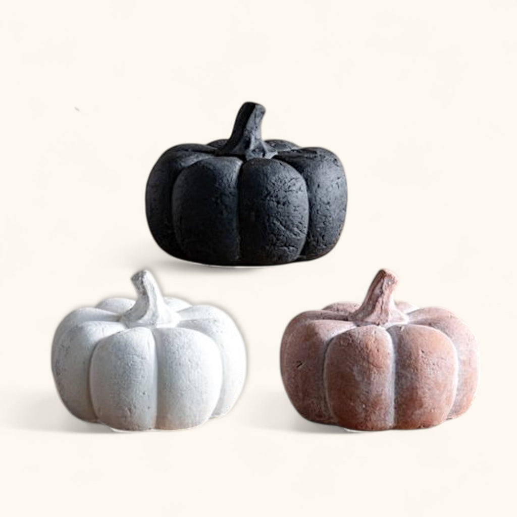 Three ceramic pumpkins in black, white, and brown on a white background