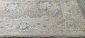A square area rug with a distressed traditional pattern in beige, cream, and muted blue-gray, featuring a fringed edge.
